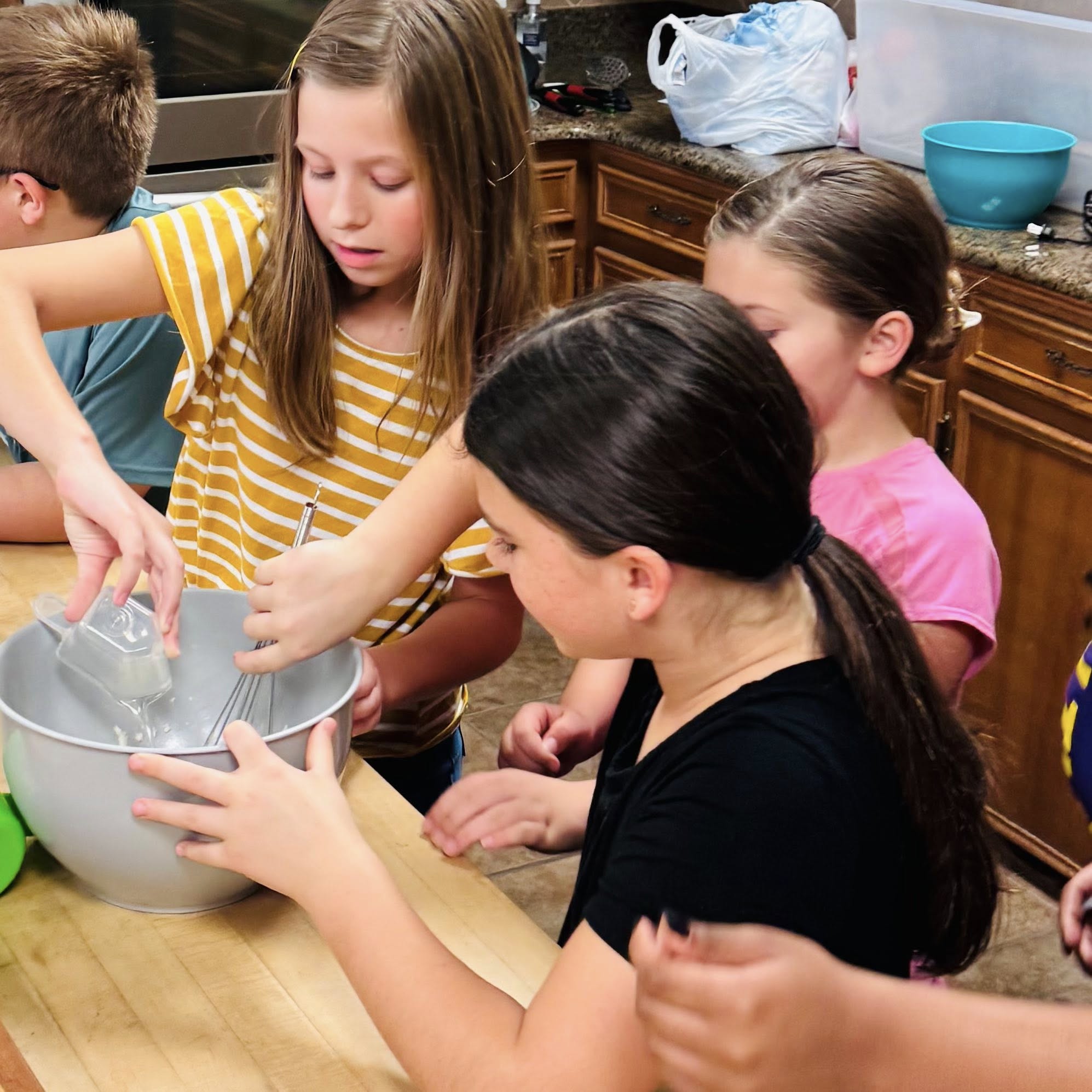 One girl pouring something in a bowl while another girl is whisking it.